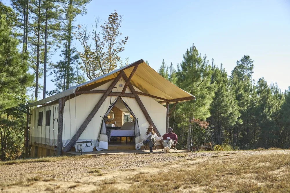 Two-person tent with a wooden frame pitched in a pine forest